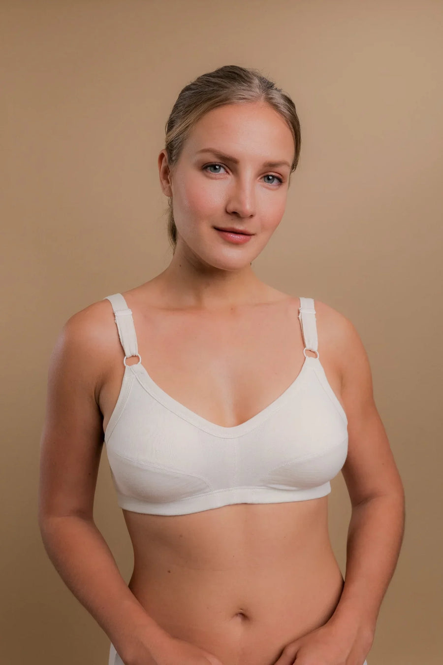 Woman wearing a white organic cotton wireless bra for sensitive skin against beige background