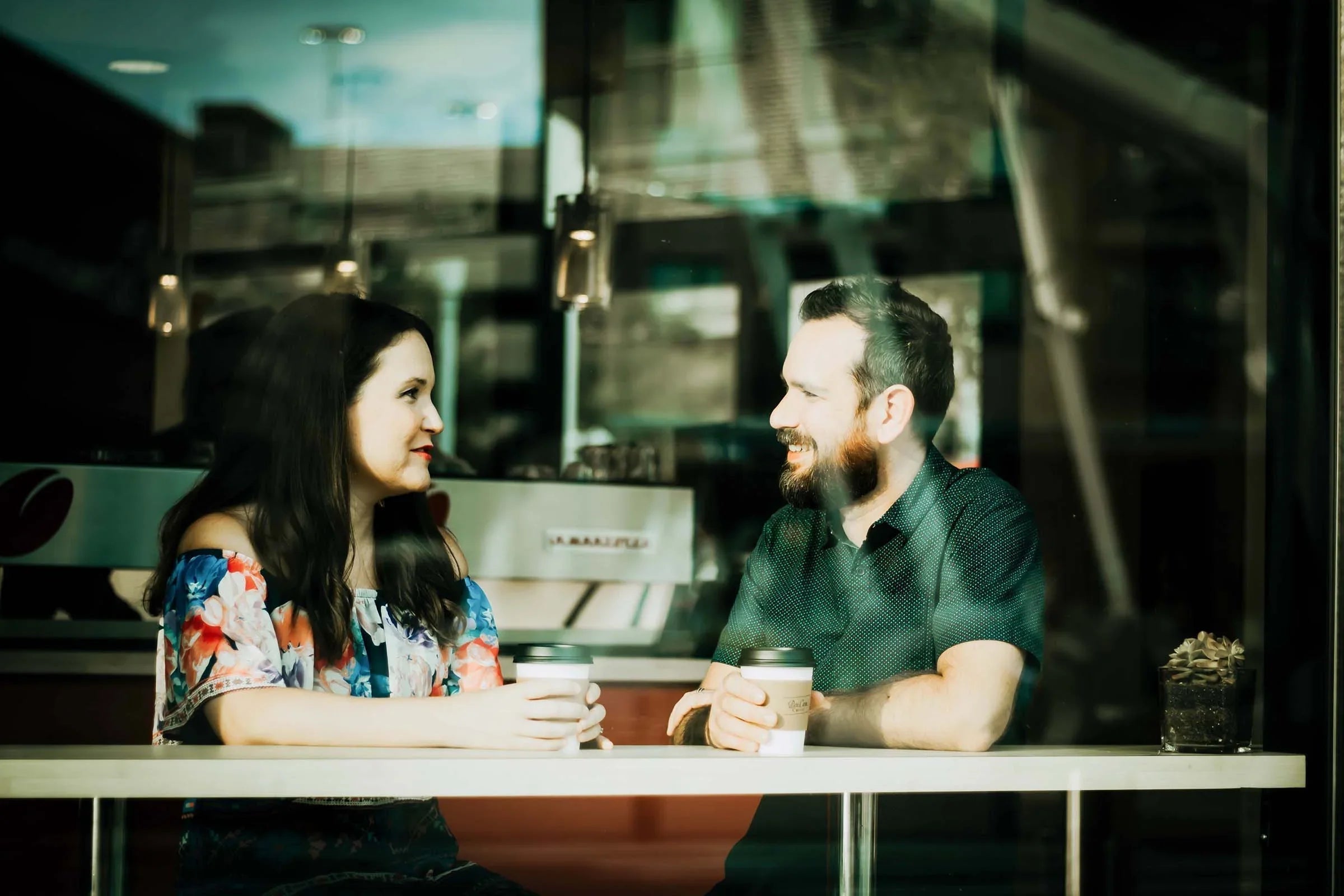Man and woman sitting in a cafe, talking and holding coffee cups