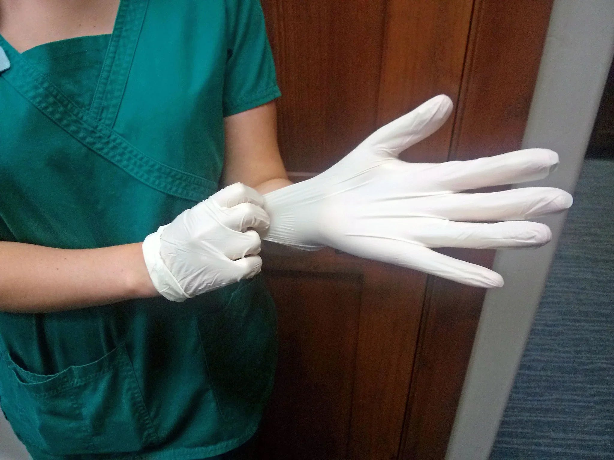 Person in green scrubs putting on white latex gloves, suitable for sensitive skin care