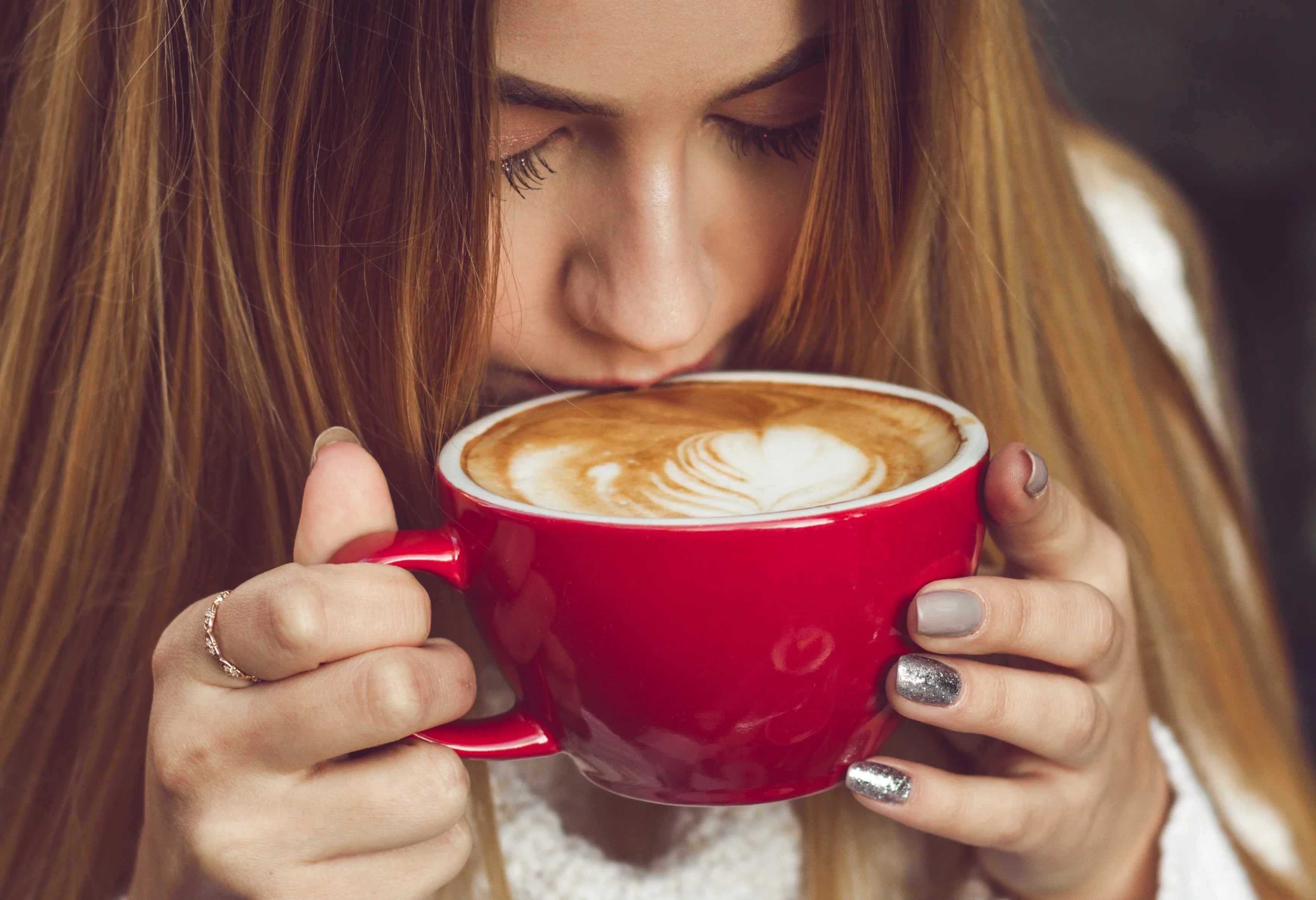 Woman in hypoallergenic cotton sweater holding a red mug of latte with latte art