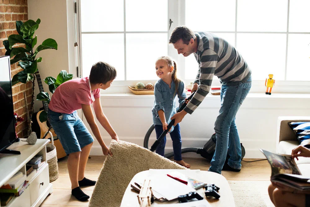 Family cleaning living room together, vacuuming carpet, child lifting rug, cozy home with sunlight