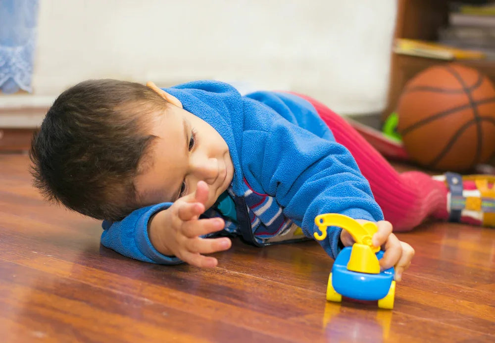 Child in hypoallergenic blue fleece jacket playing with toy on hardwood floor, basketball in background