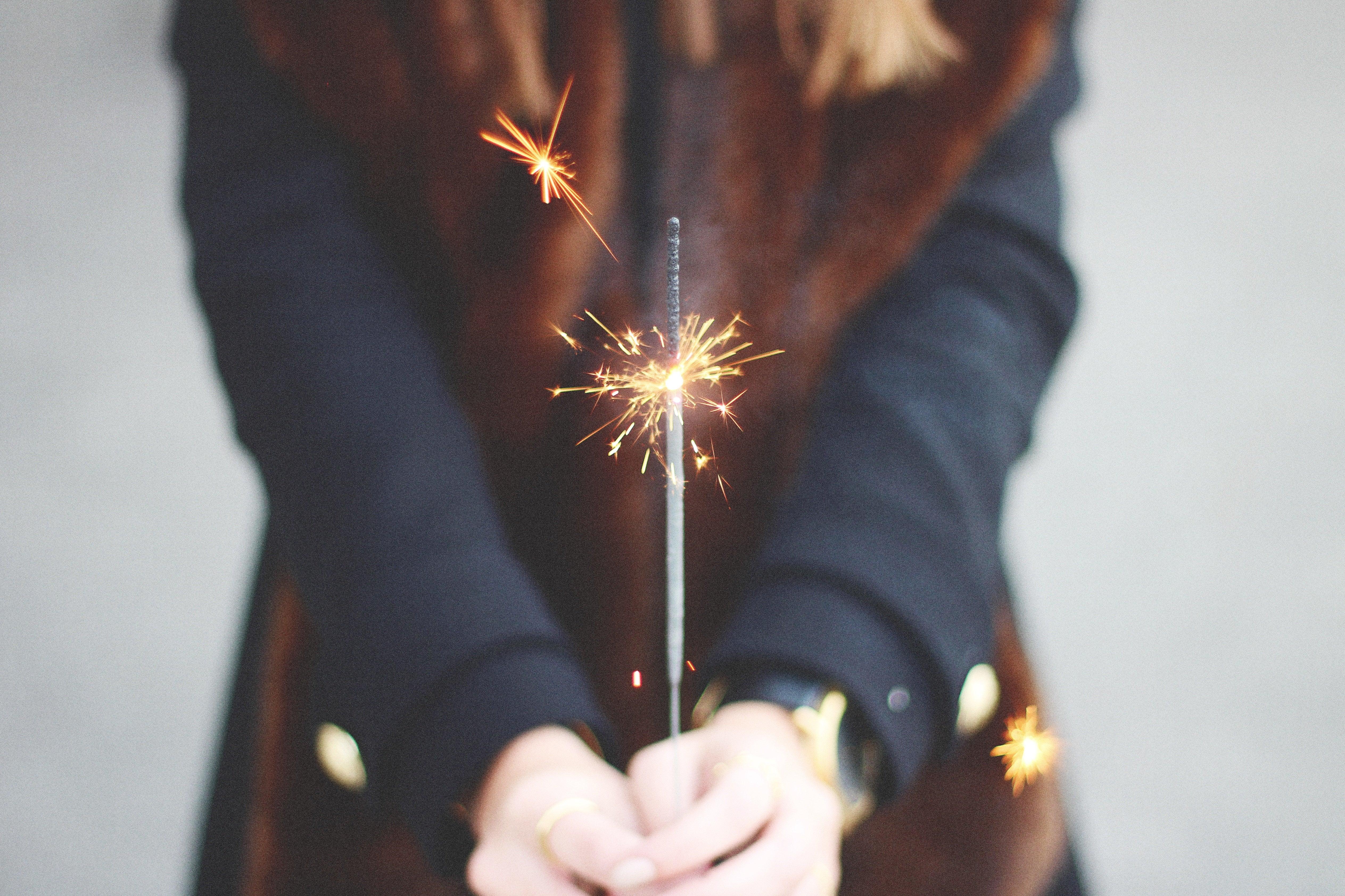 Person in dark sleeve holding a lit sparkler, celebrating, focus on hands and sparkling light