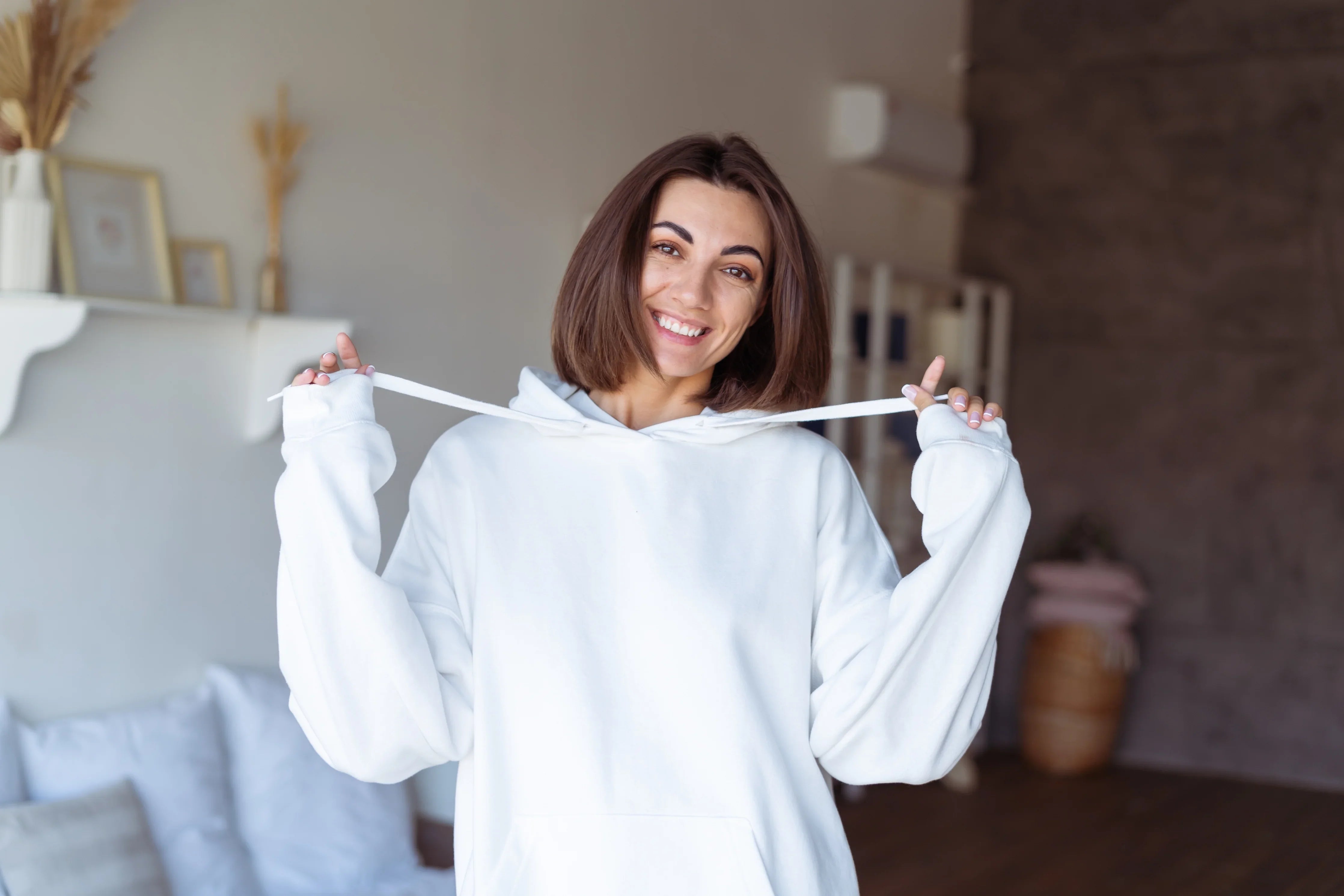 Smiling woman in a white hypoallergenic Cottonique hoodie in a cozy bedroom setting