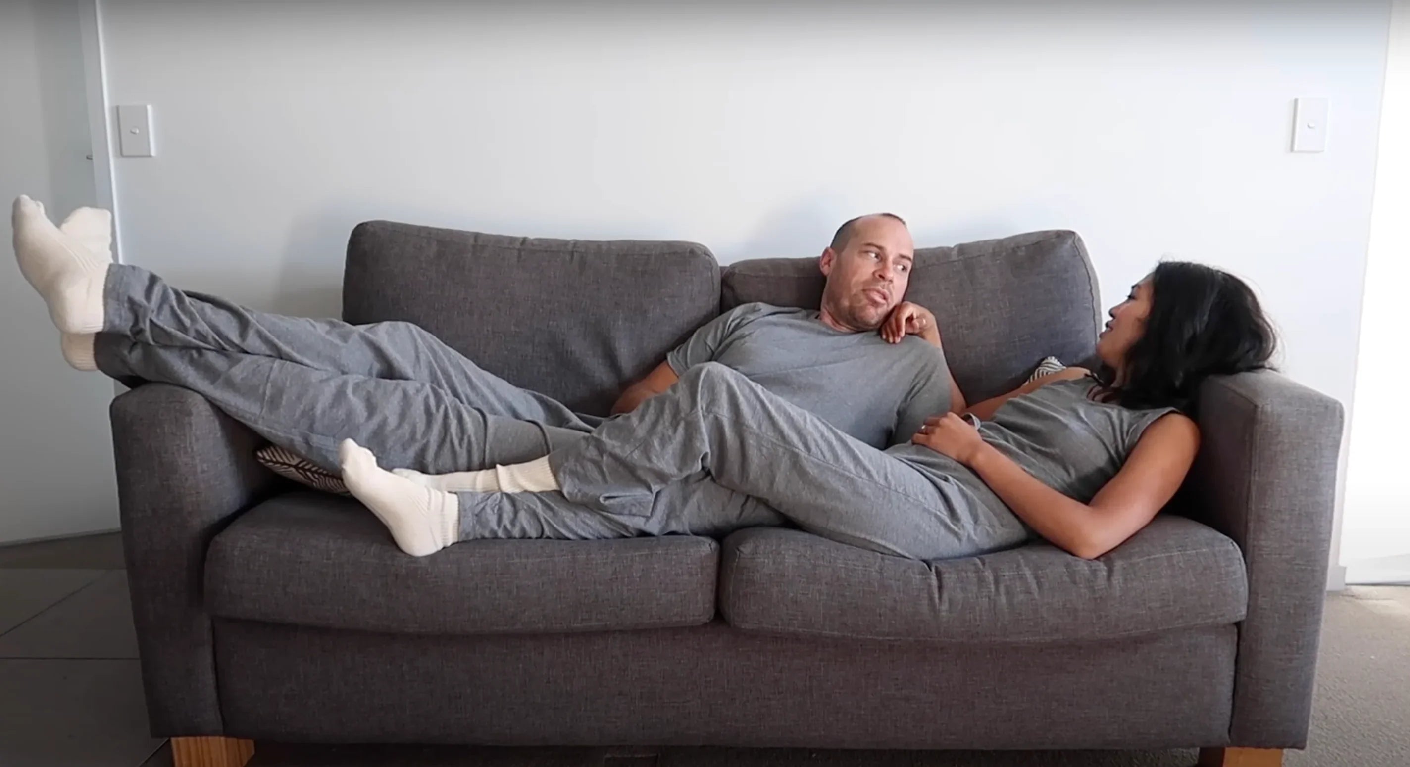 Man and woman relaxing on grey sofa wearing allergy-free hypoallergenic Cottonique loungewear