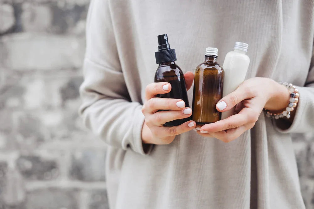 Person in neutral sweater holding brown and white bottles, hypoallergenic skincare theme