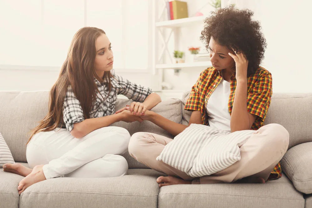 Two women in casual cotton clothing sitting on a couch, offering comfort and support