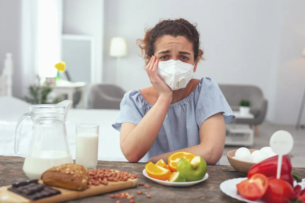Woman with allergy mask surrounded by common food allergens like milk, eggs, nuts, and fruit