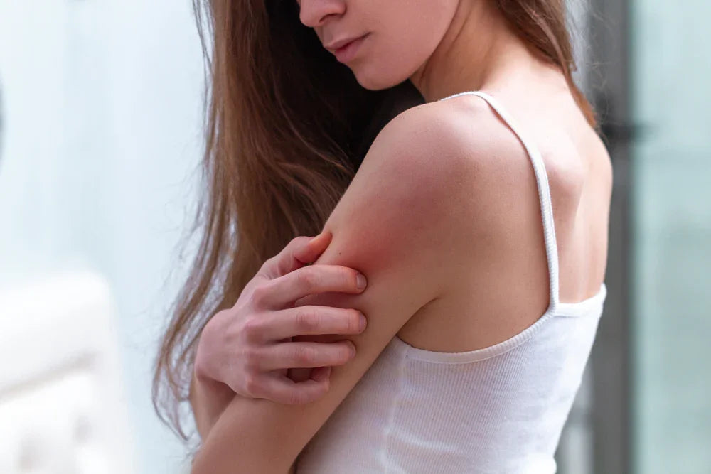Woman in white tank top scratching red irritated skin, allergy-free apparel concept