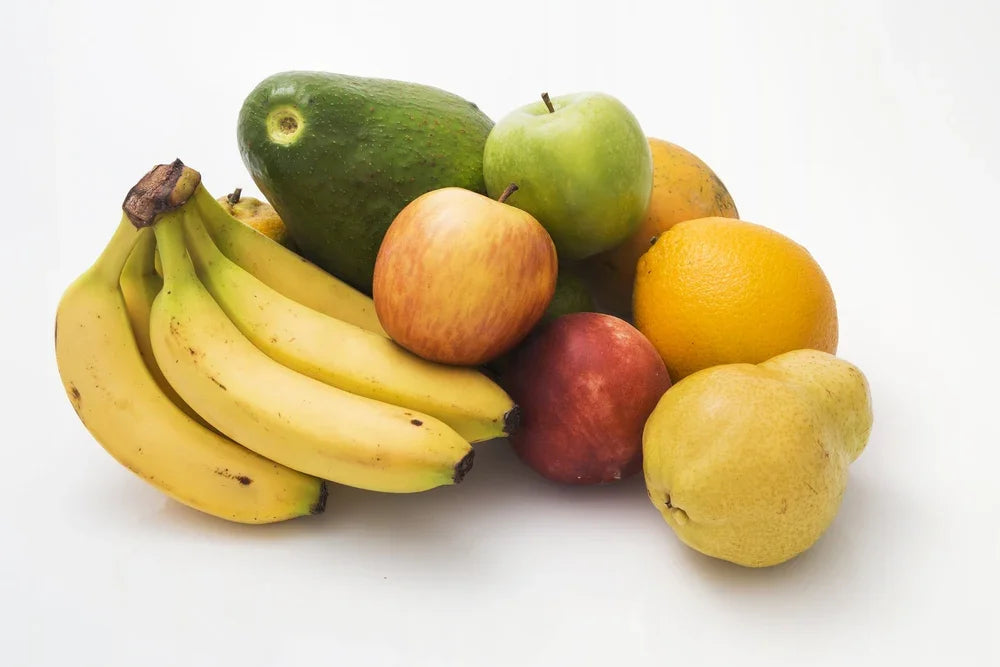 Assorted fresh fruit including bananas, apples, pear, orange, and avocado on white background