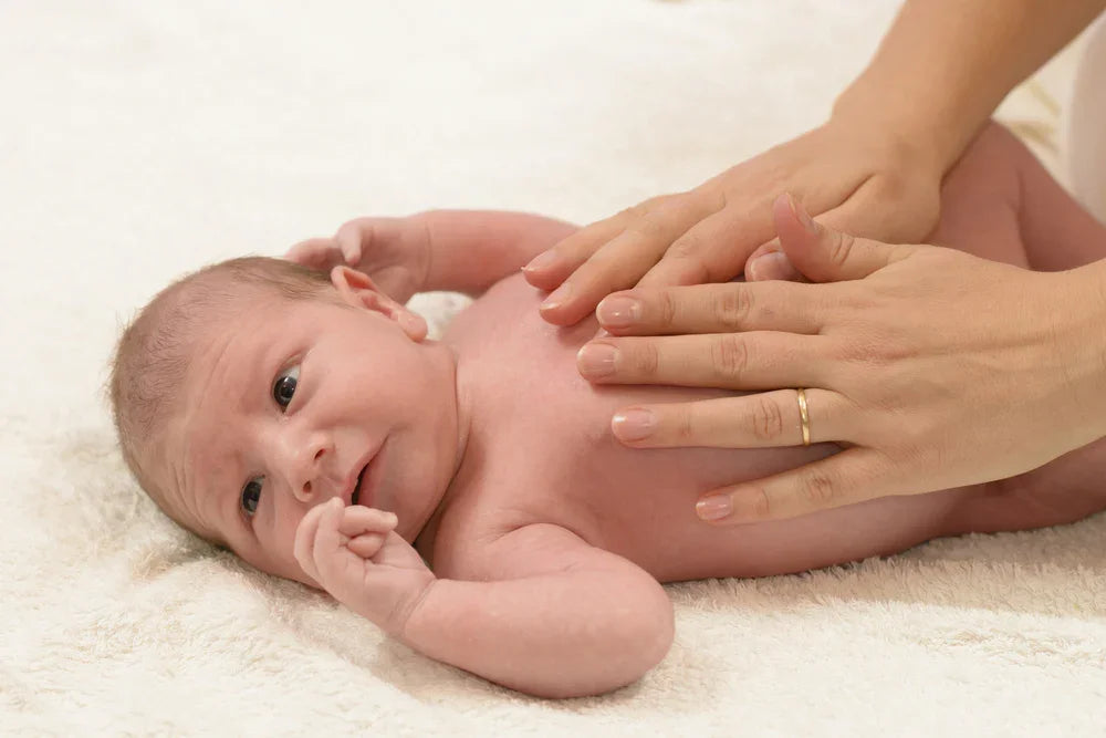 Hands gently massaging a newborn baby on a soft white fabric background, sensitive skin care