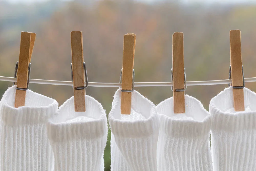 White organic cotton socks hanging on a clothesline with clothespins outdoors
