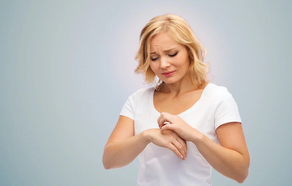 Woman in white shirt scratching wrist, showing skin irritation, allergy-free apparel concept