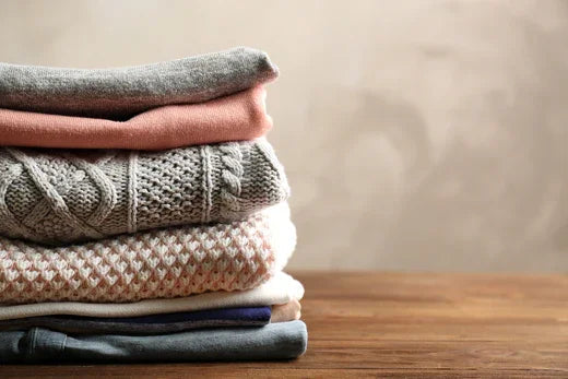 Stack of allergy-free cotton sweaters on a wooden table, Cottonique hypoallergenic apparel