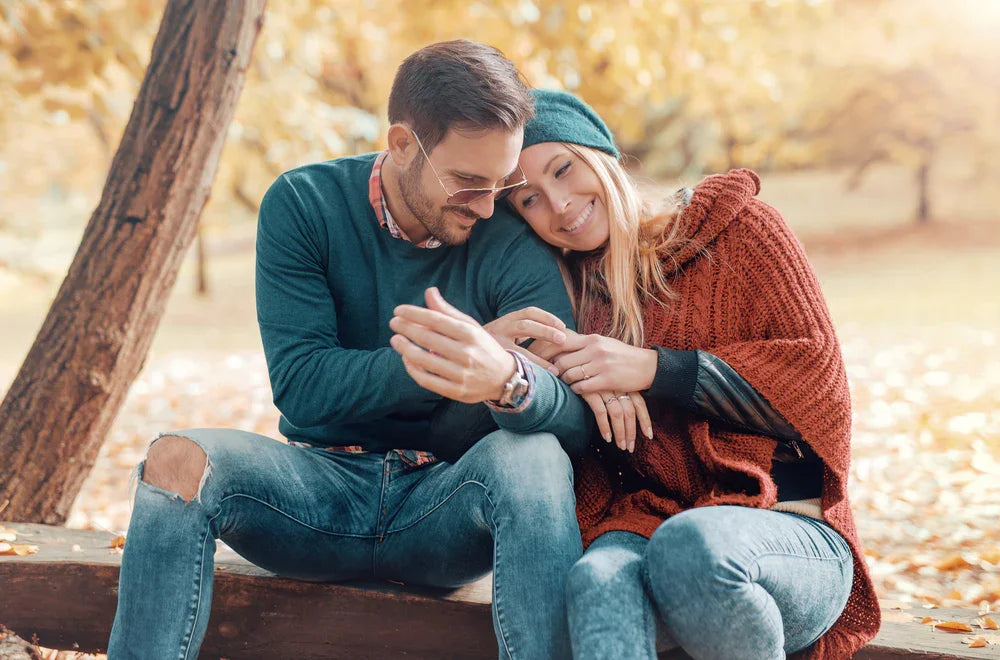 Happy couple in soft knit sweaters and jeans sitting on a bench in an autumn park
