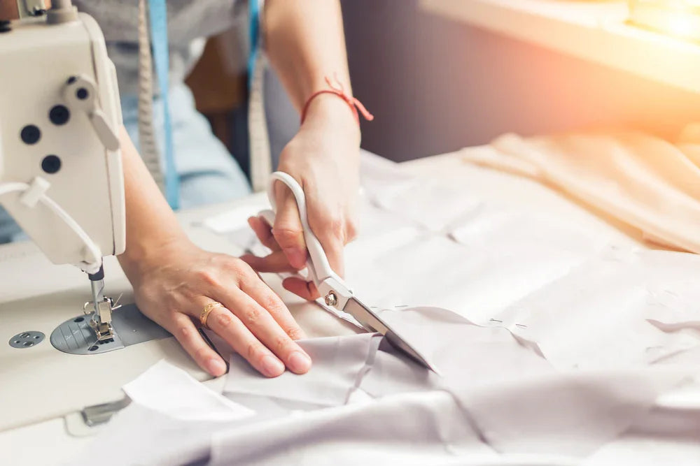 Person cutting organic cotton fabric next to a sewing machine, allergy-free clothing production
