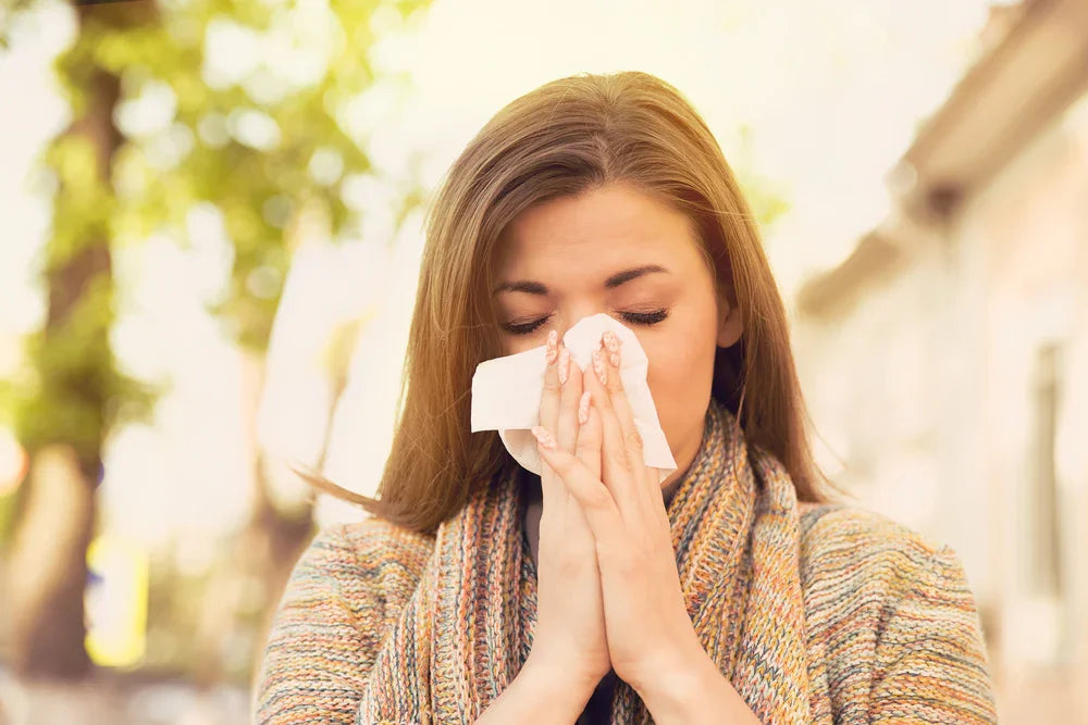 Woman outdoors with tissue sneezing, wearing allergy-friendly knit sweater