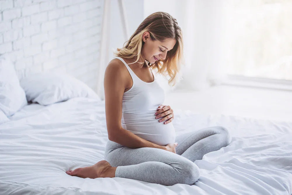 Pregnant woman in hypoallergenic cotton loungewear sitting on bed in bright bedroom