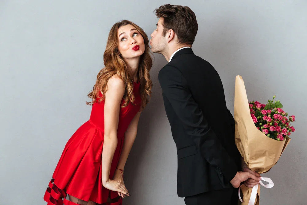 Man in suit holding bouquet behind back, woman in red dress smiling, allergy-free apparel
