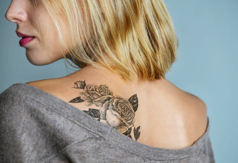 Woman with short blonde hair showing rose tattoo on upper back, wearing grey allergy-free top