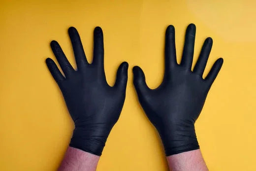 Hands wearing black gloves on yellow background, allergy-safe protective clothing
