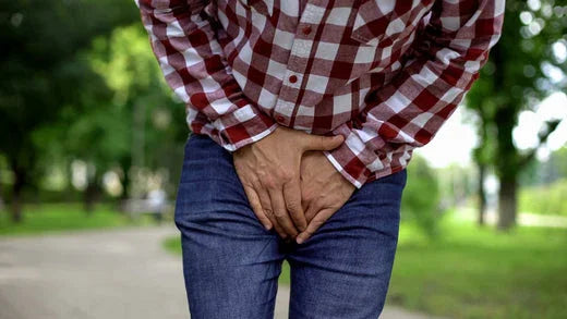 Person in plaid shirt and jeans outdoors holding pelvic area, showing discomfort or irritation