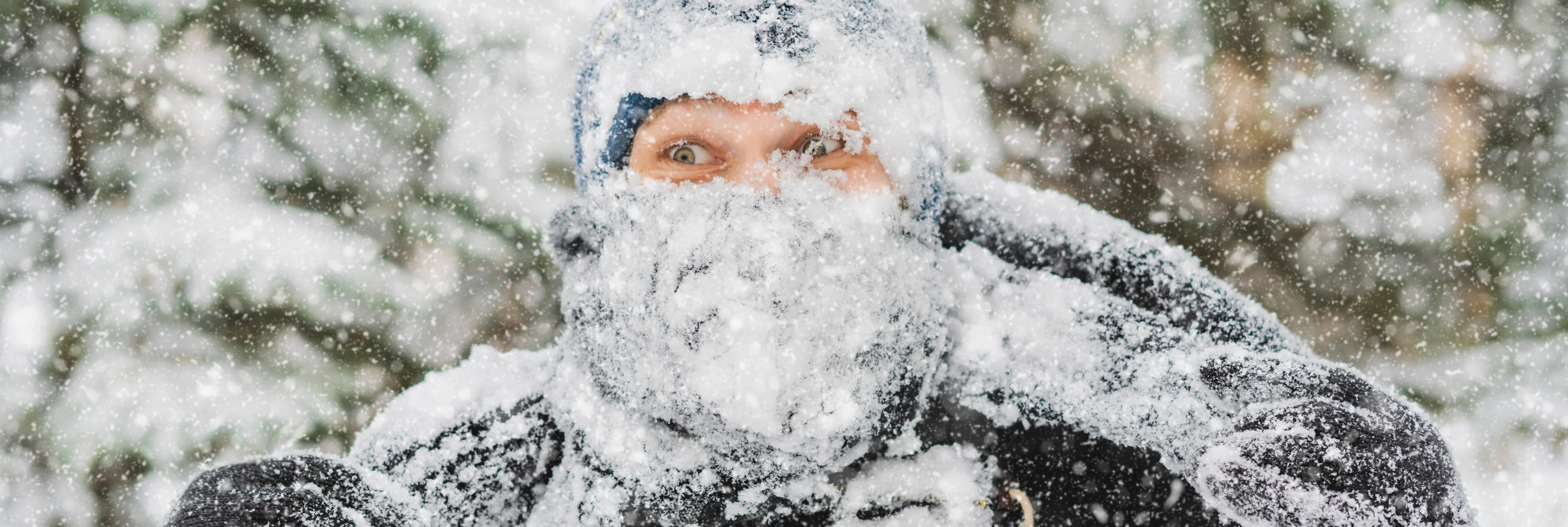Person bundled in winter apparel covered in snow, outdoors during heavy snowfall