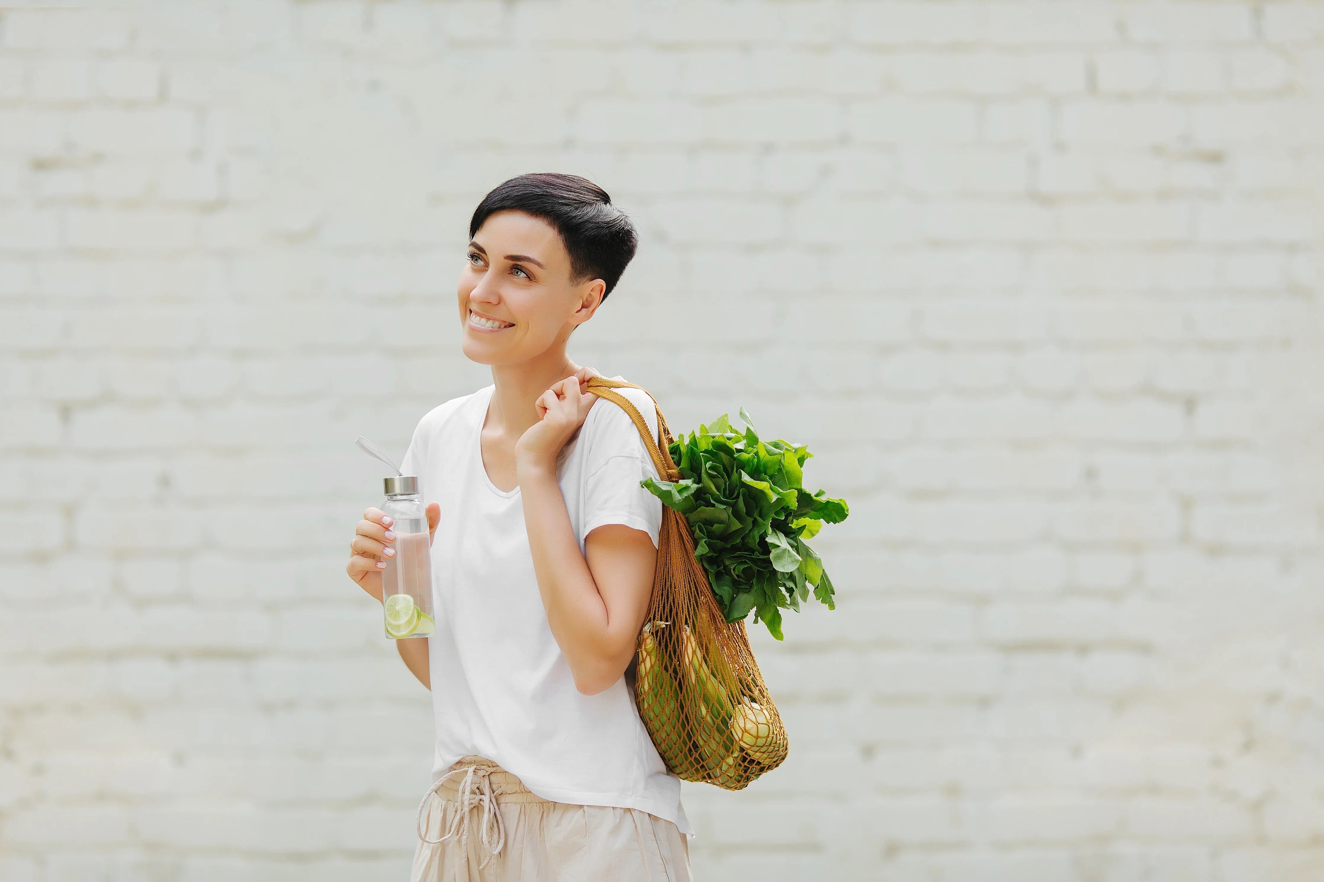 Woman in allergy-free cotton t-shirt holding reusable bag with greens and water bottle