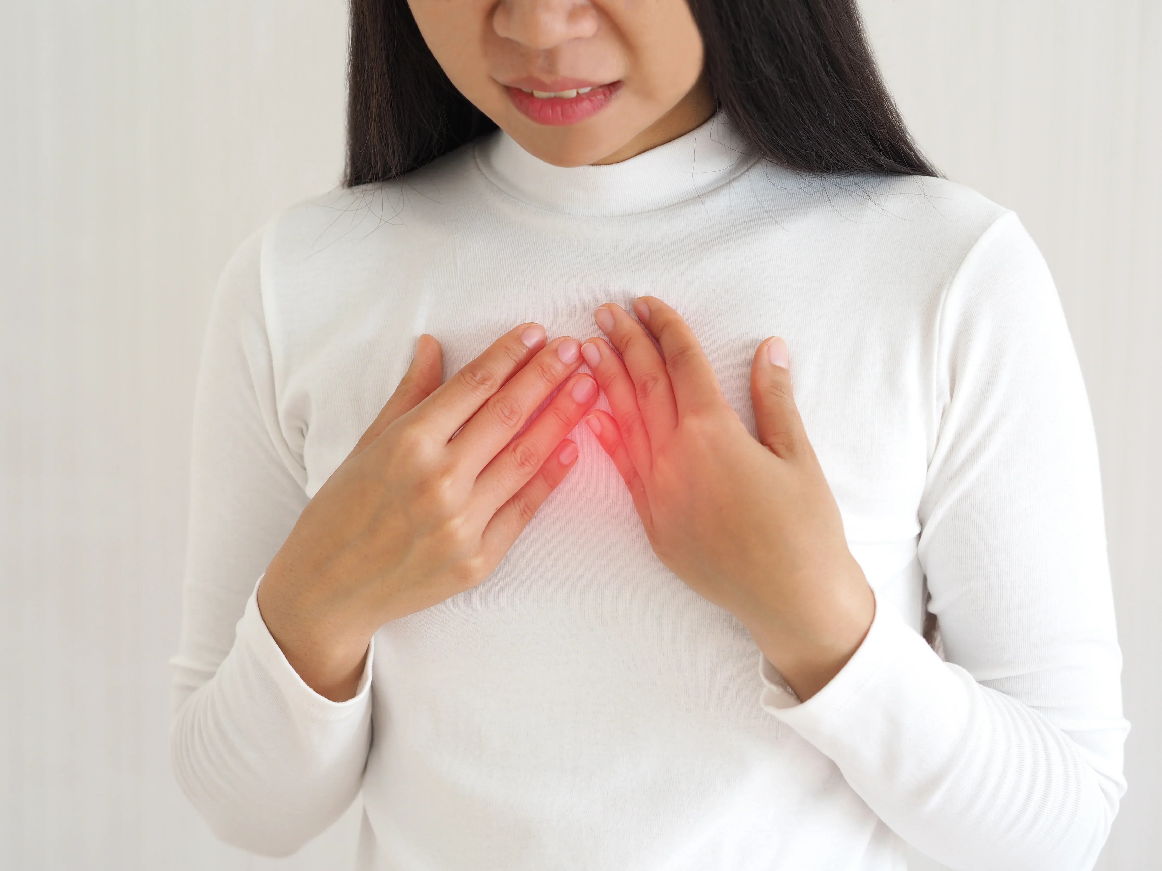 Woman in white long sleeve shirt touching chest, highlighting sensitive skin irritation