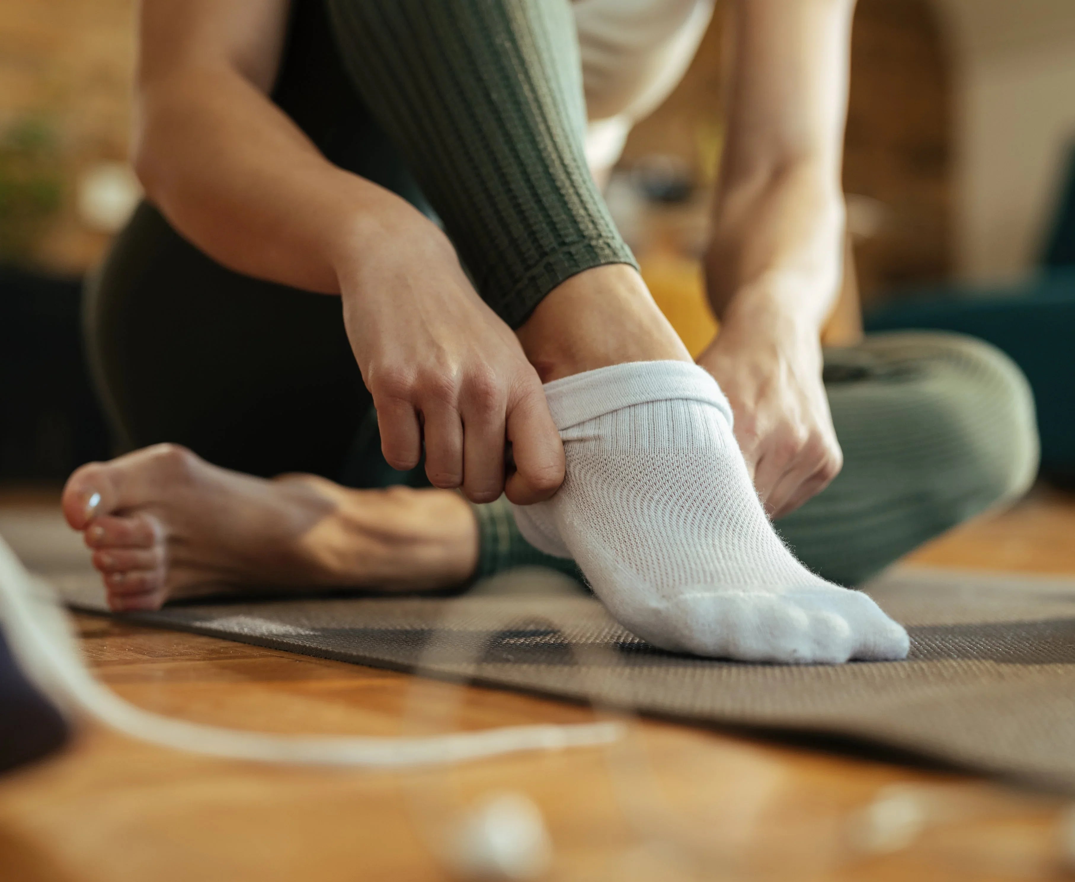 Woman putting on soft white organic cotton socks for sensitive skin while sitting indoors