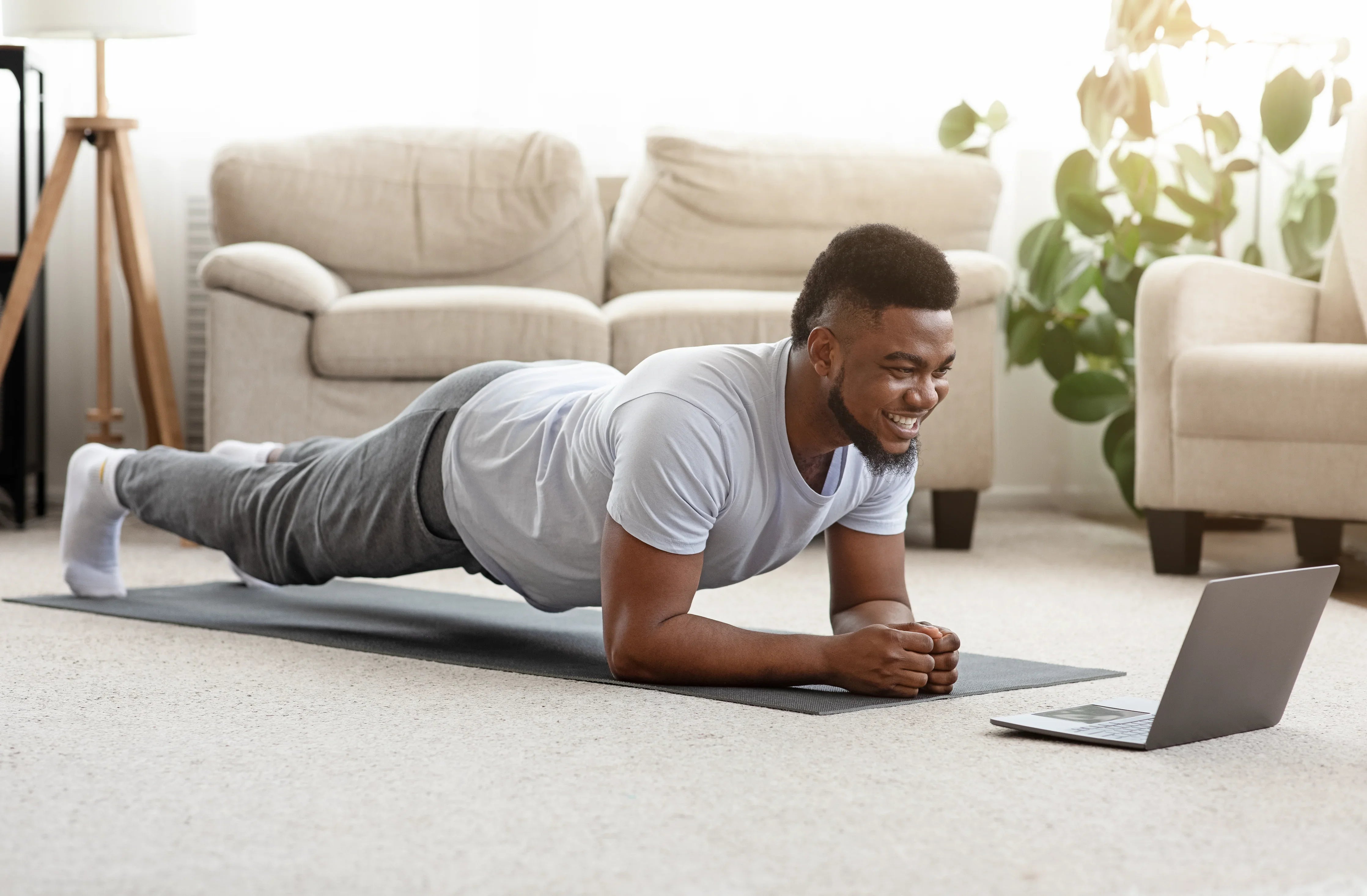Man in hypoallergenic cotton shirt and pants exercising at home on mat, watching laptop