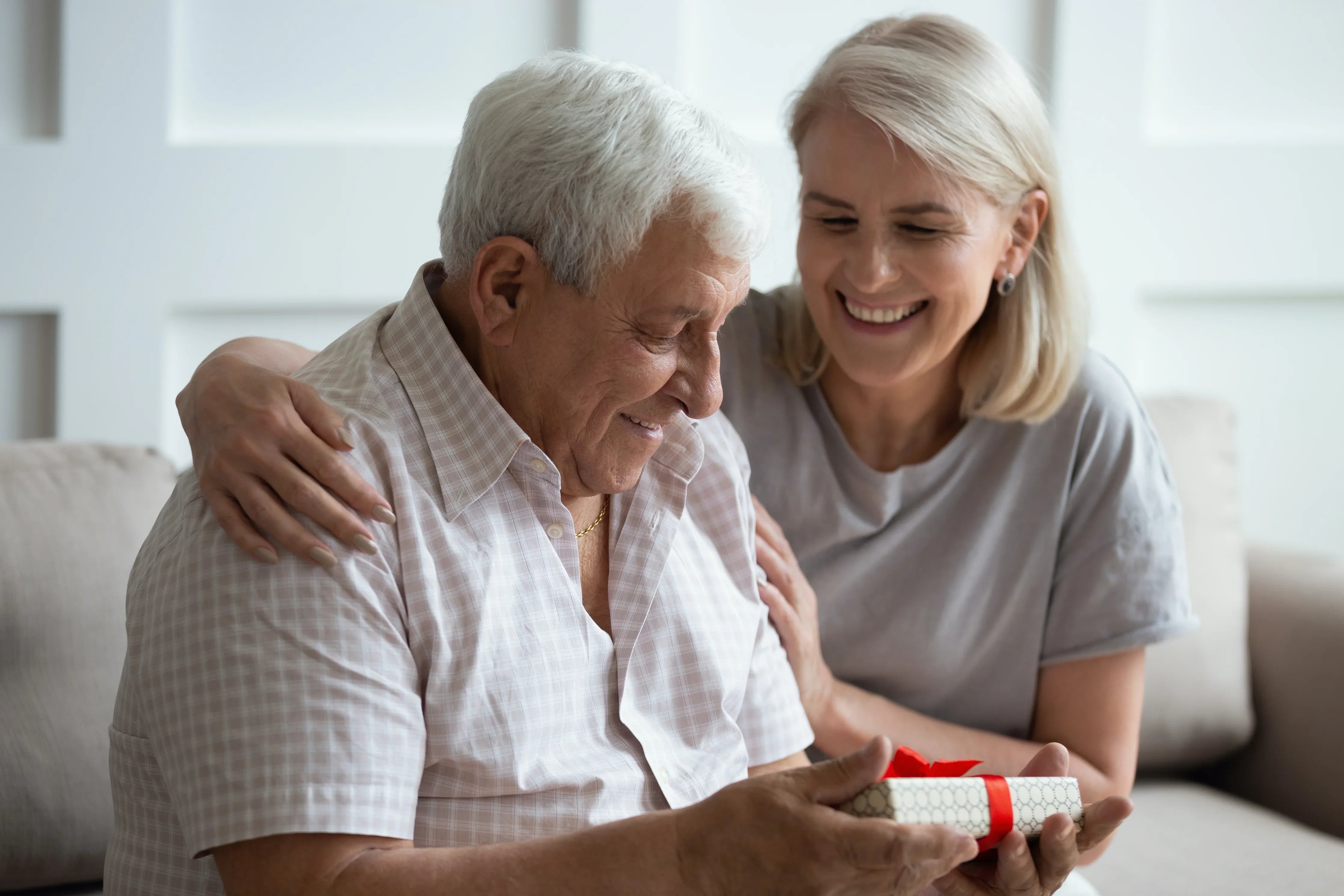 Smiling older man receiving a small gift box from a woman, both in soft cotton clothing