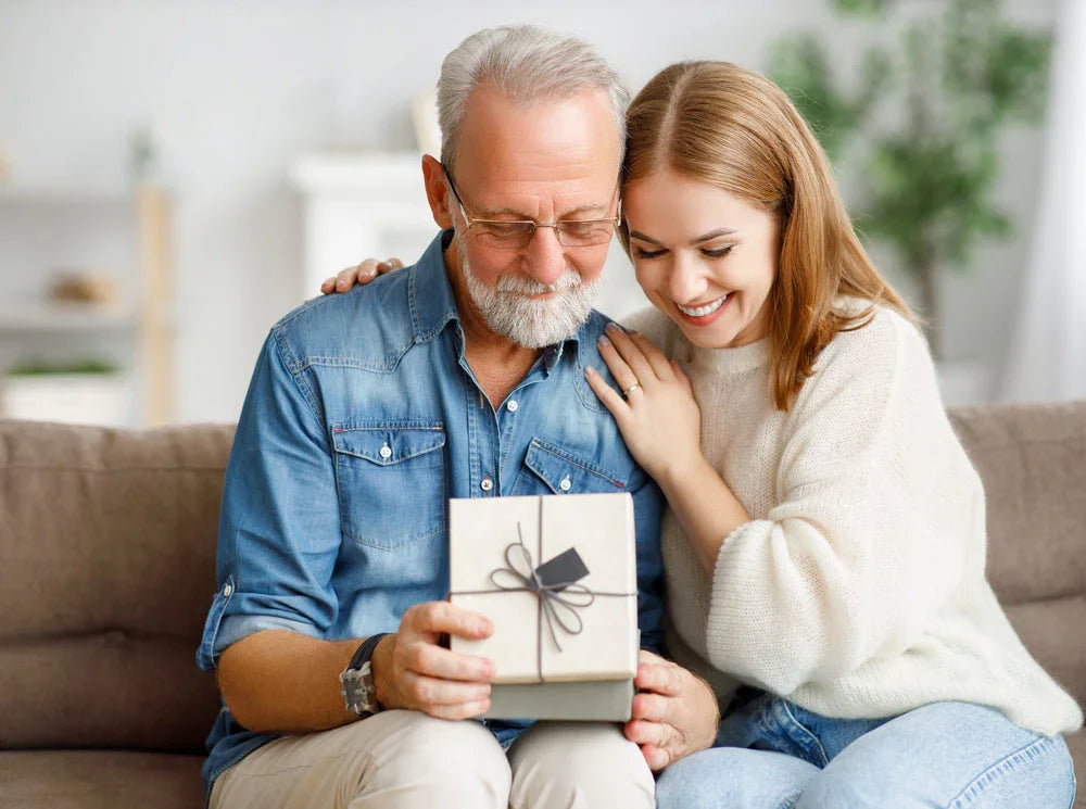 Happy woman giving elderly man a wrapped gift box on a cozy sofa at home