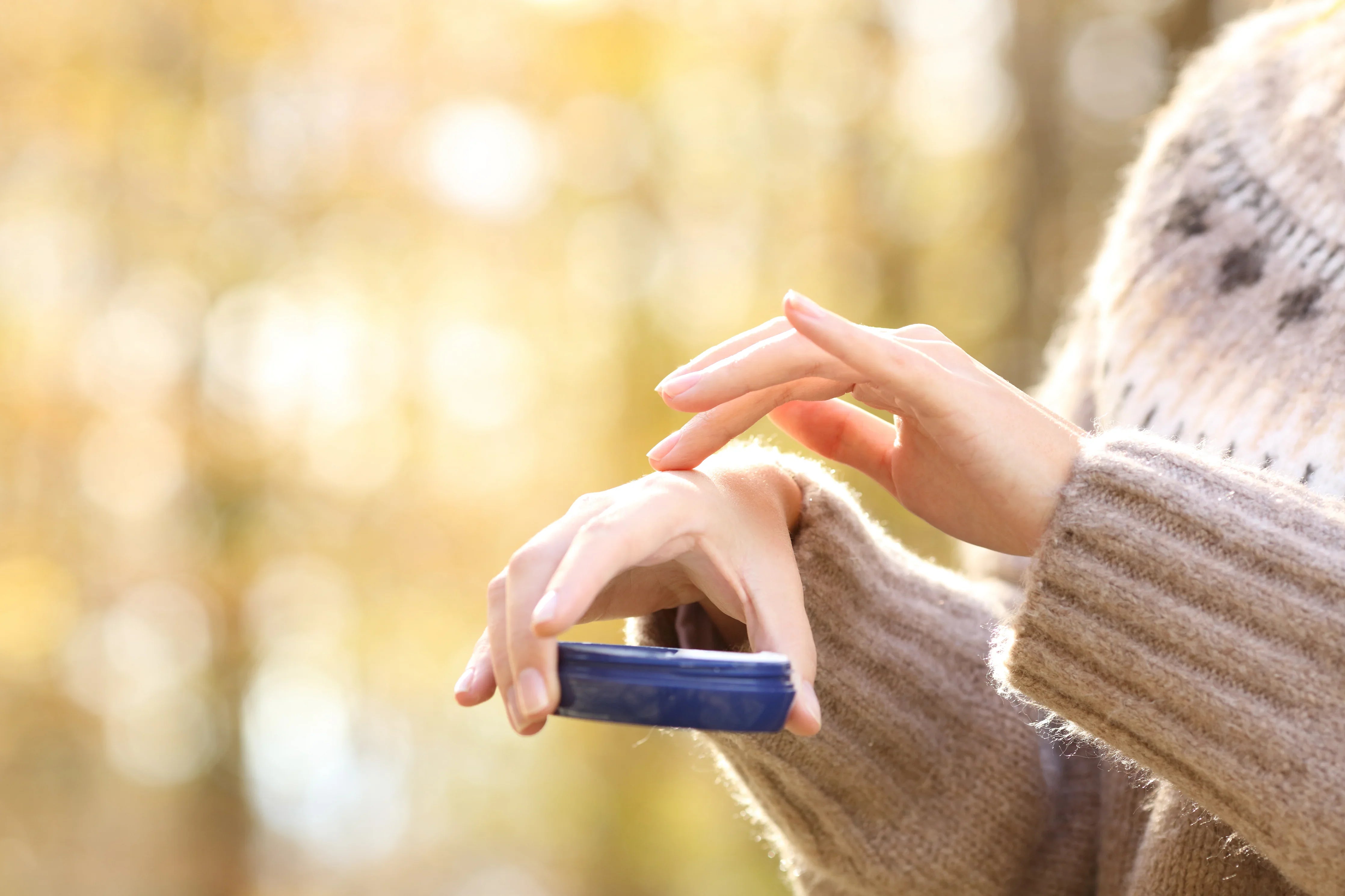 Person in allergy-free cotton sweater applying cream to hands outdoors
