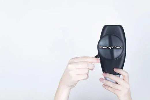 Hands holding a black bottle labeled phenoxyethanol against a plain background