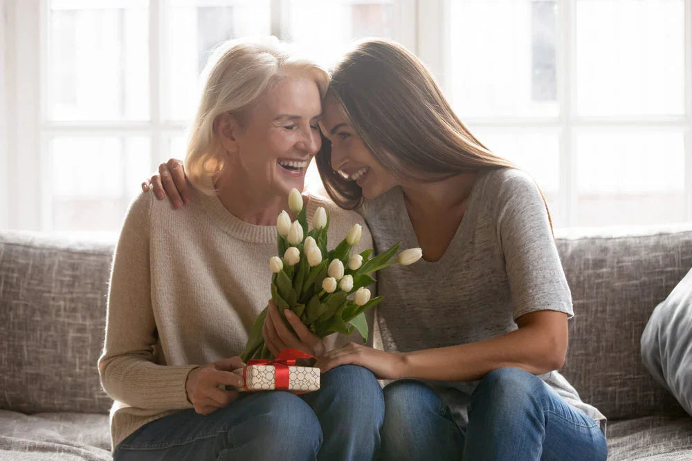 Smiling women on couch with white tulips and gift, wearing allergy-free Cottonique apparel