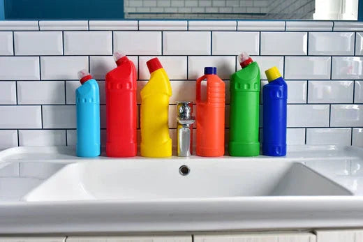 Colorful plastic detergent bottles on white tiled bathroom sink, allergy-free cleaning theme.
