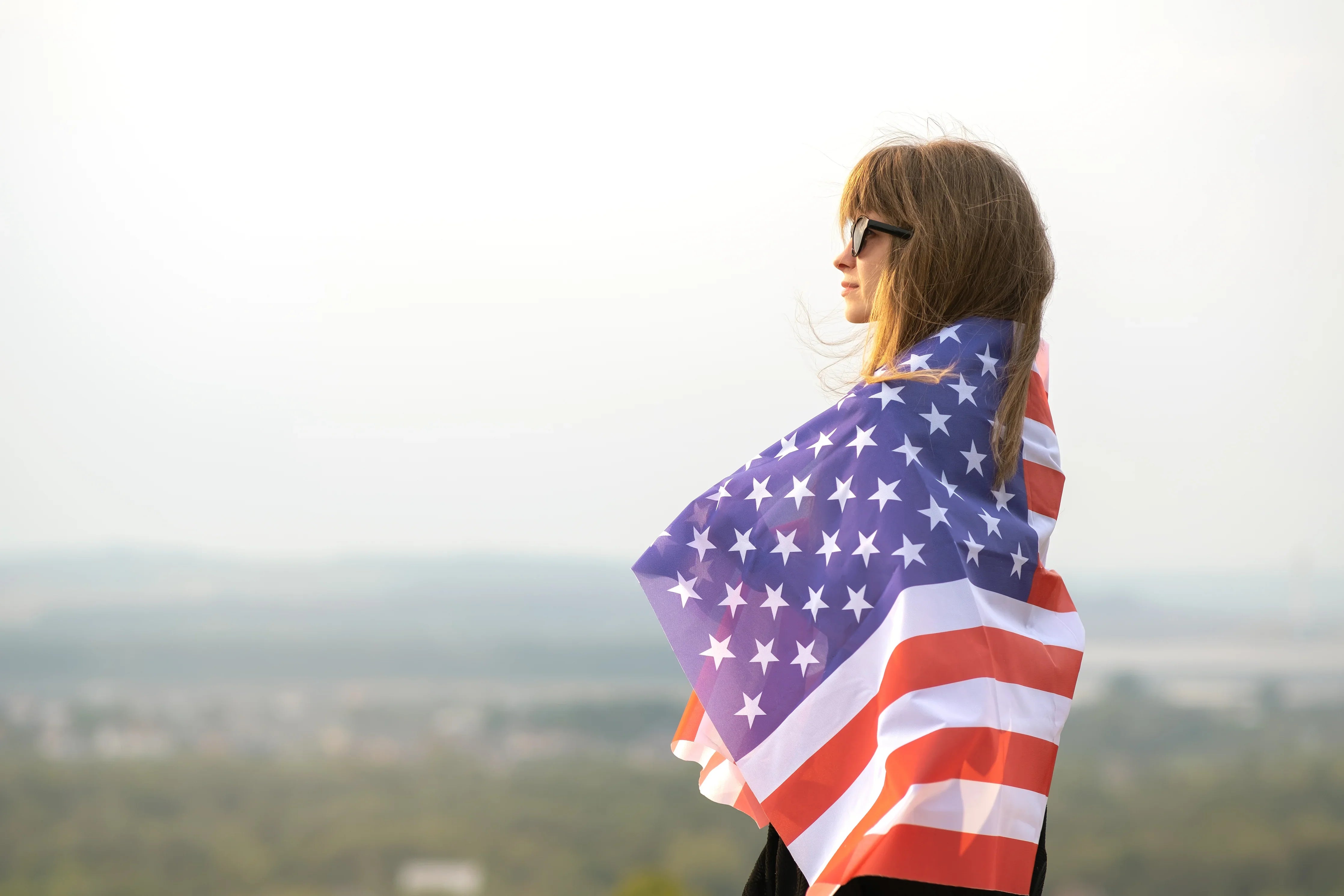 Woman wearing sunglasses wrapped in American flag outdoors, hypoallergenic apparel concept