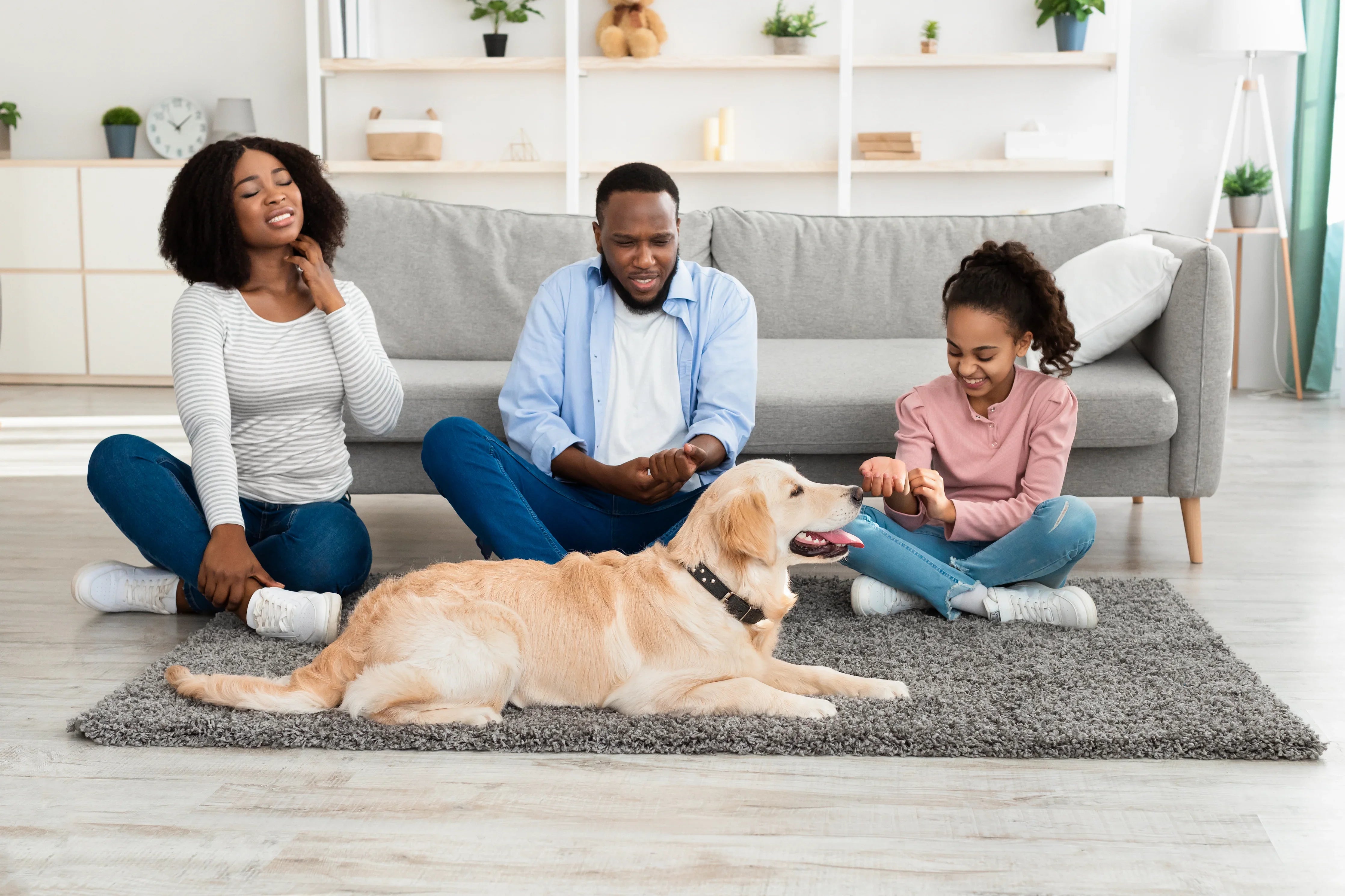 Family of three and golden retriever on living room carpet, woman scratching neck, allergy-free apparel