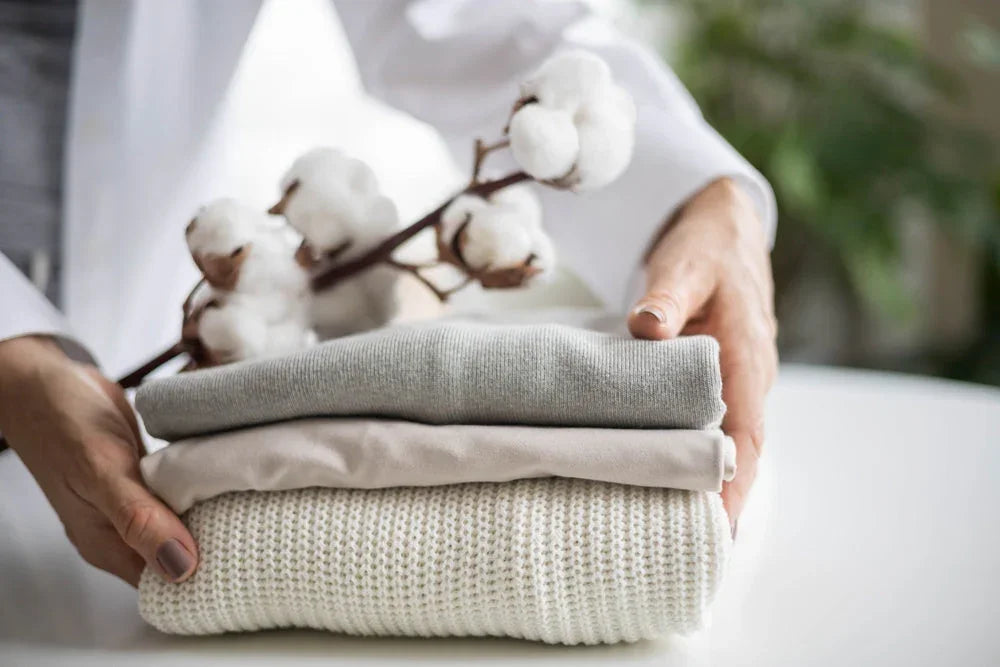 Hands holding folded allergy-free cotton clothing with a cotton branch, Cottonique apparel