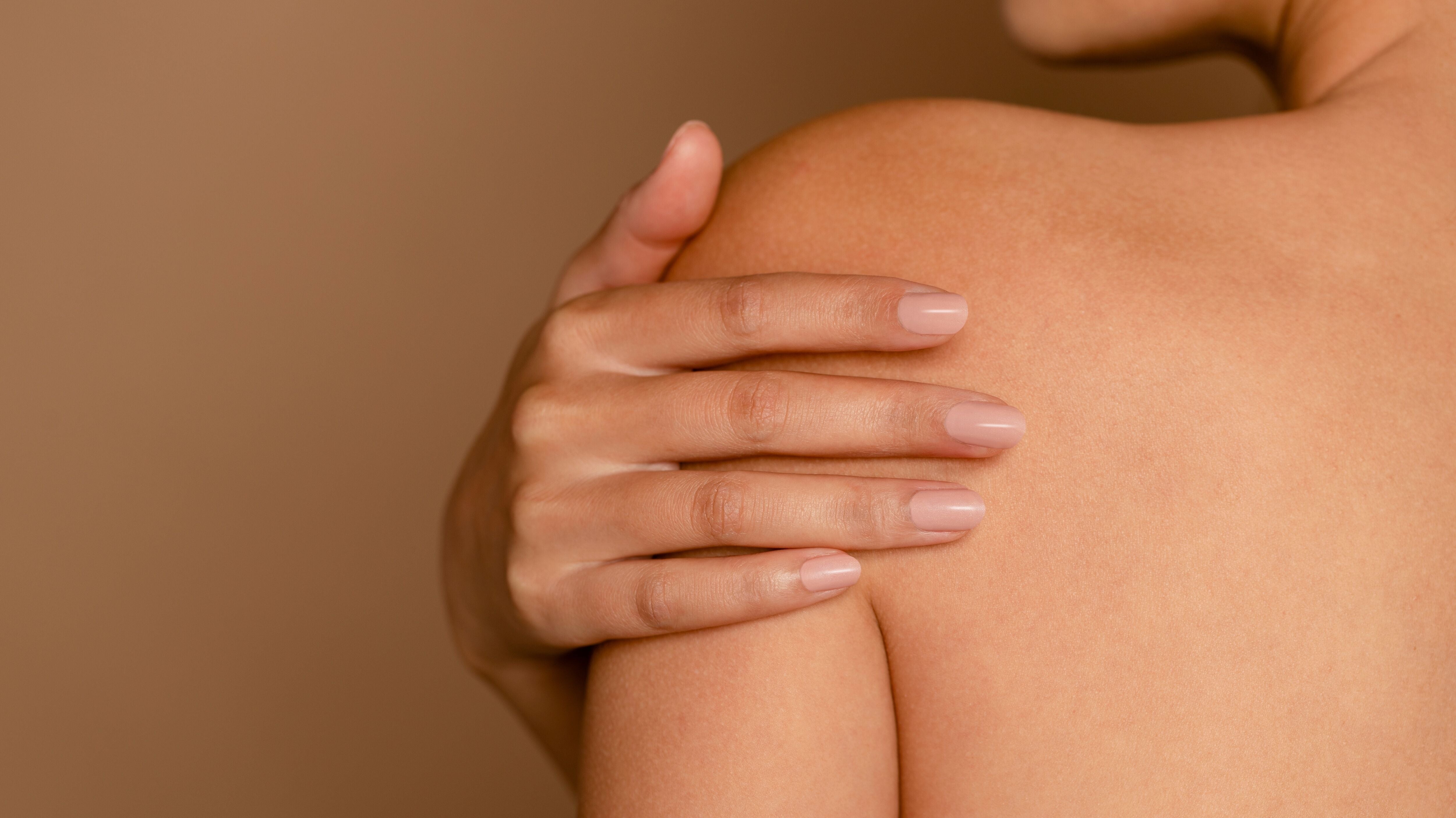 Close-up of a person touching their bare shoulder and back, highlighting sensitive skin.