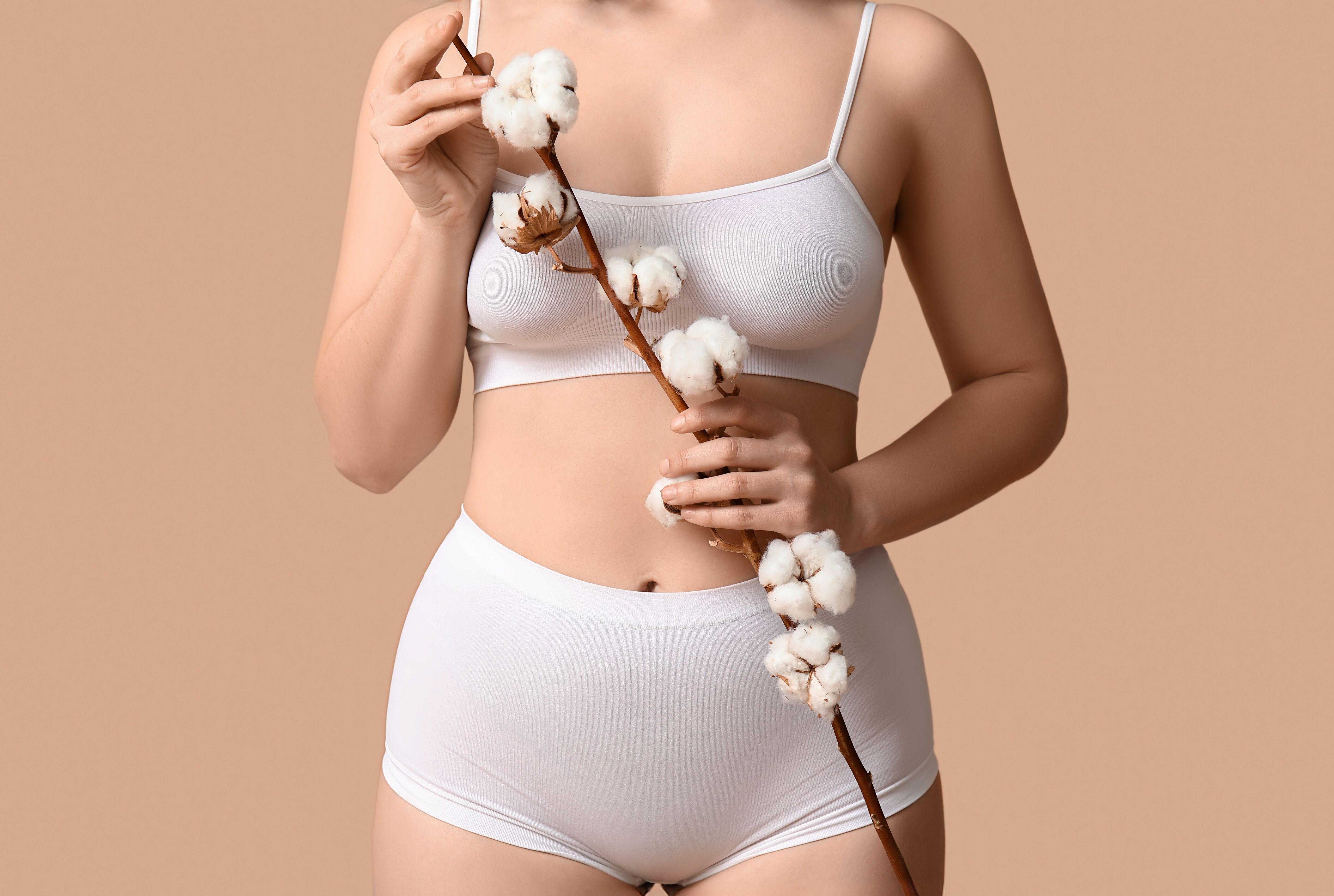 Woman wearing white organic cotton underwear holding cotton plant on neutral background