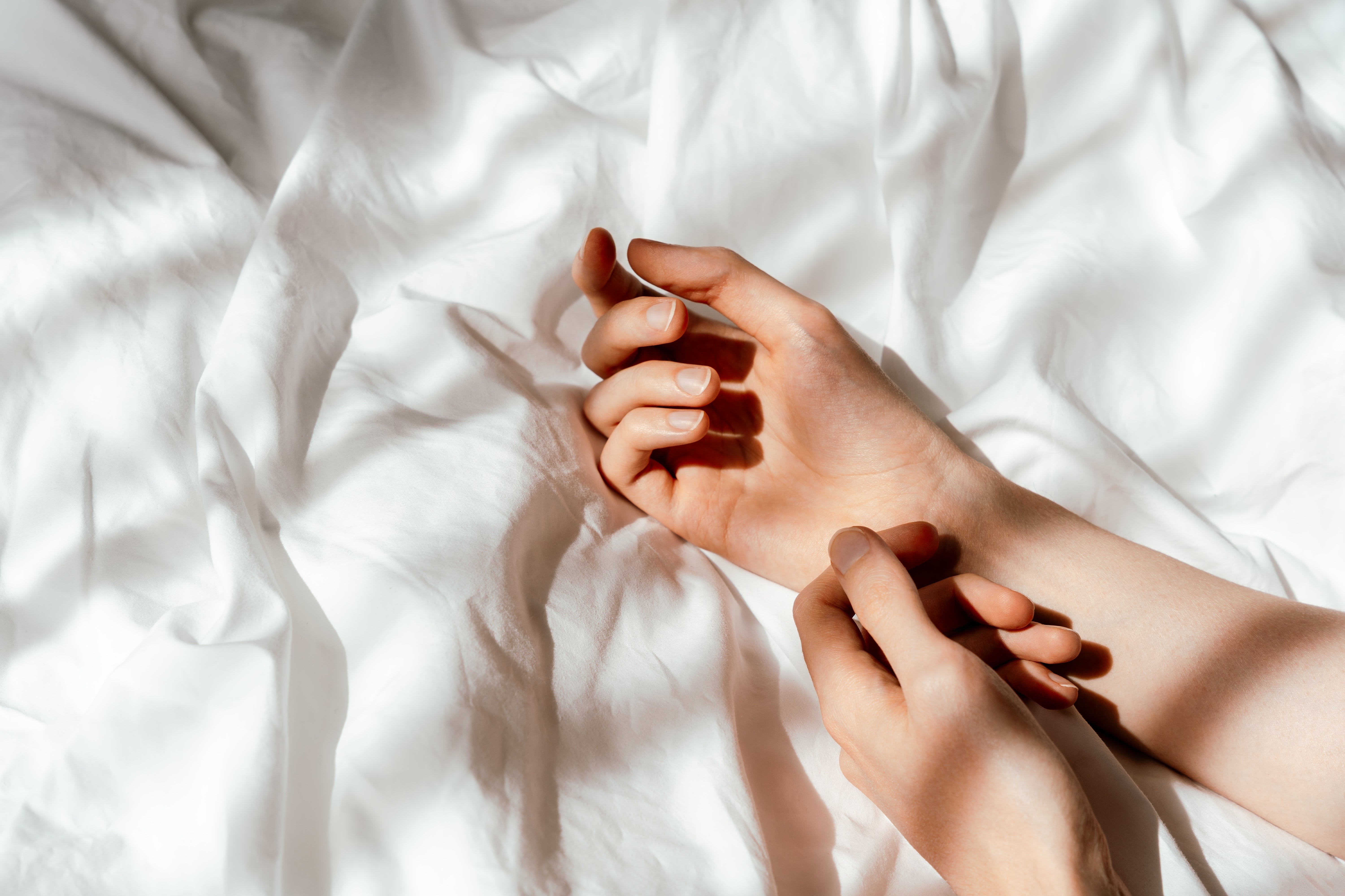 Close-up of a person scratching their wrist on white hypoallergenic bedding