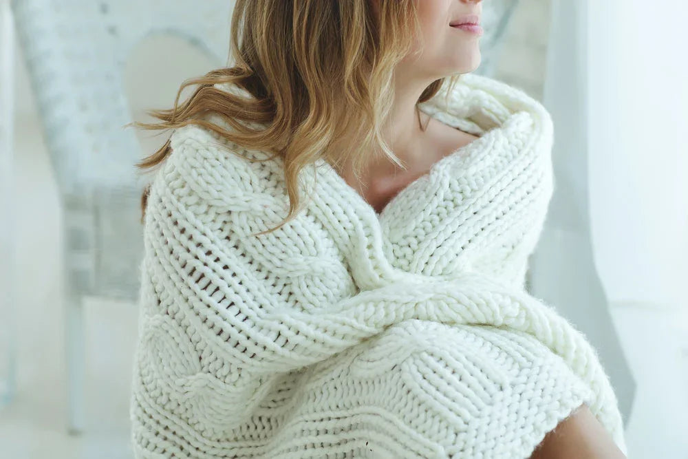 Woman wrapped in a chunky white knit blanket, showcasing cozy hypoallergenic comfort