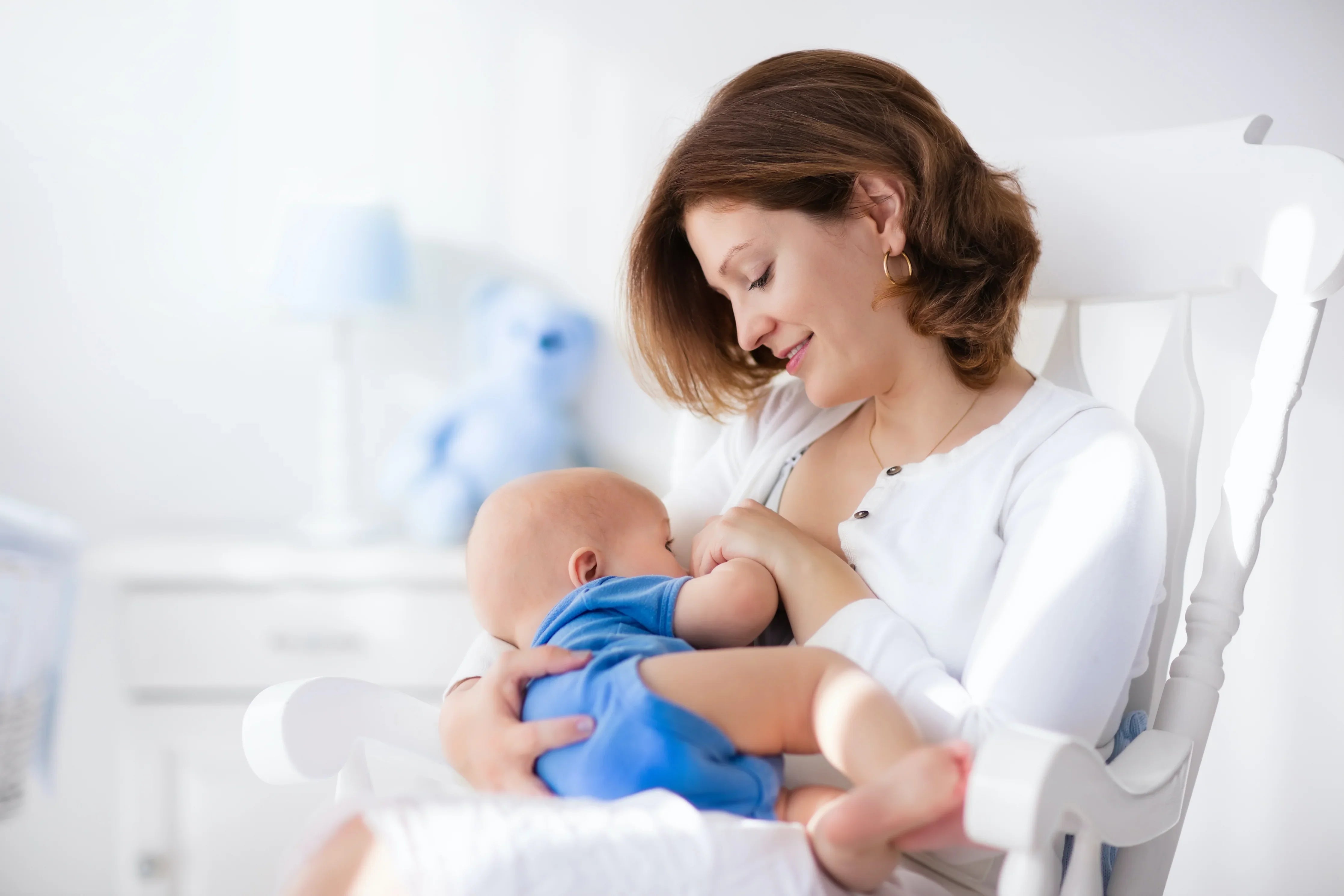 Mother breastfeeding baby in bright nursery, both wearing soft, allergy-friendly cotton clothing
