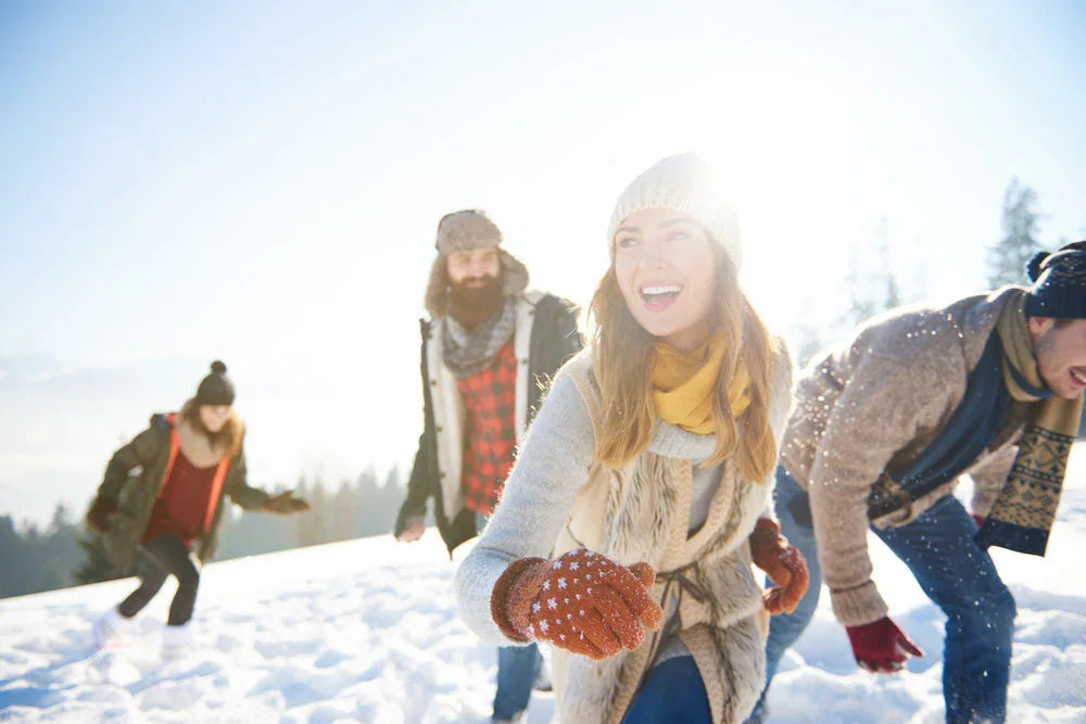 Group of adults wearing winter clothing playing in snow on a sunny day outdoors