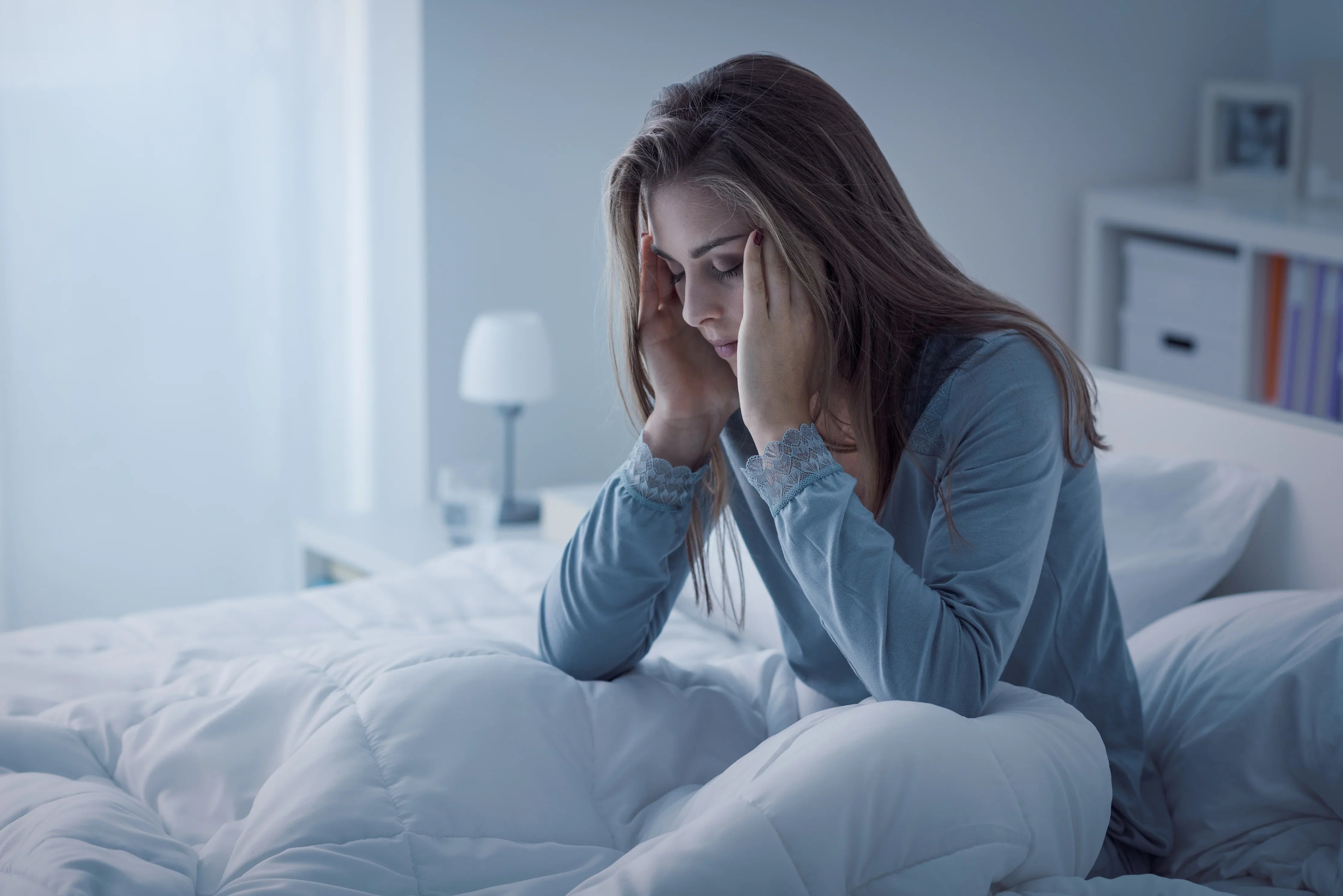 Woman in allergy-friendly cotton nightwear sitting on bed, looking tired in a bright bedroom