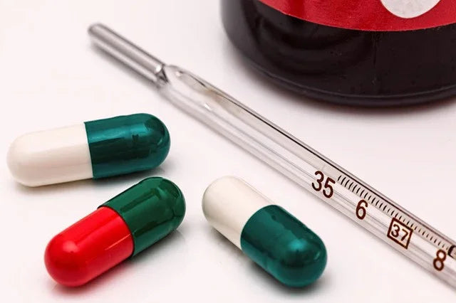 Glass thermometer and three capsules on white background, fever and flu medication concept.