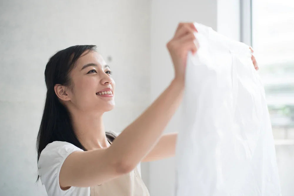 Smiling woman holding up a clean white hypoallergenic cotton shirt by a window