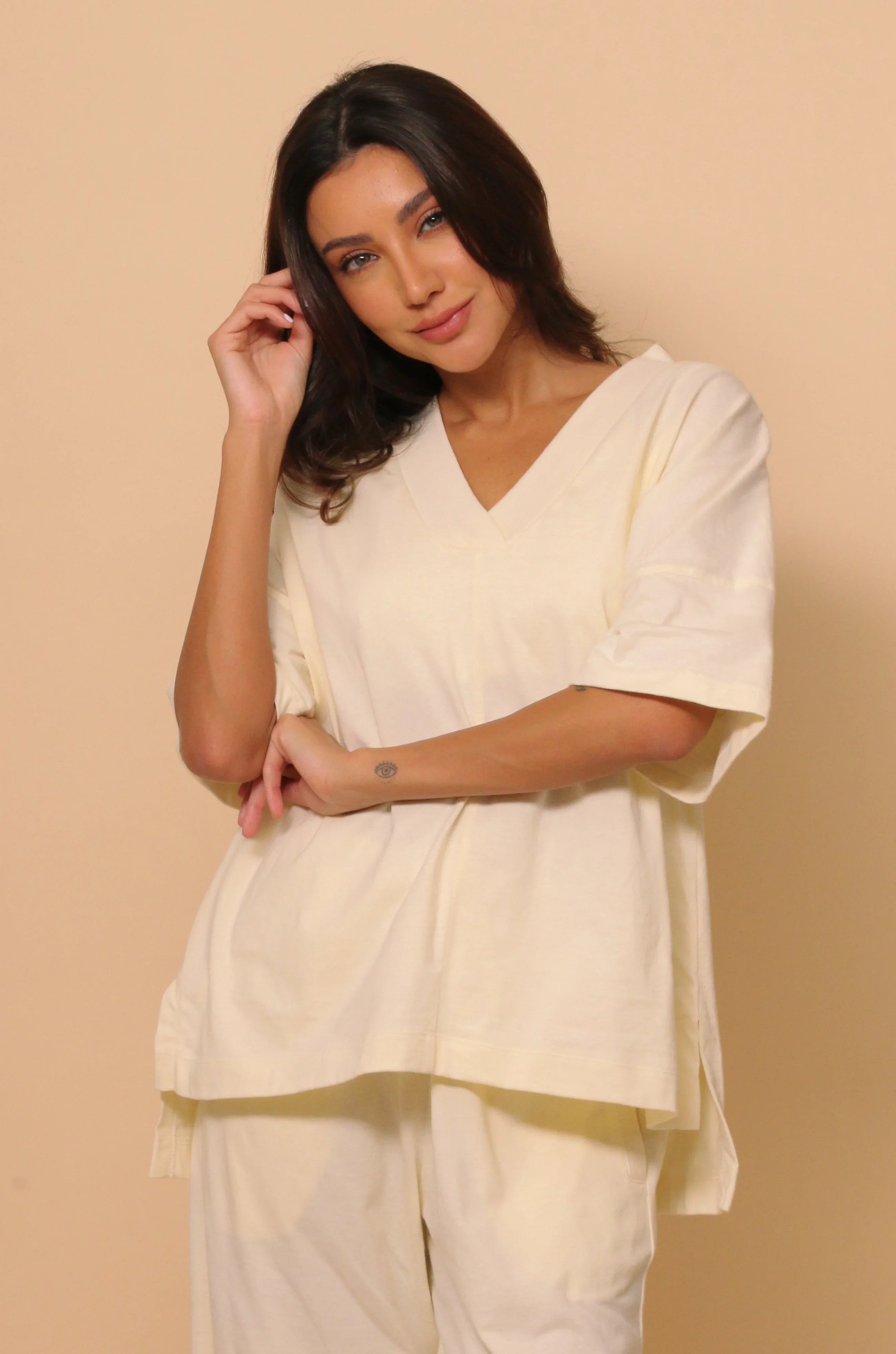 Woman in cream hypoallergenic Cottonique V-neck shirt and pants against beige background
